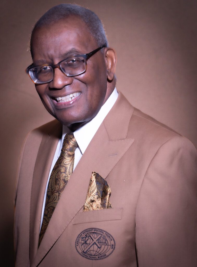 Smiling man in brown suit and glasses.