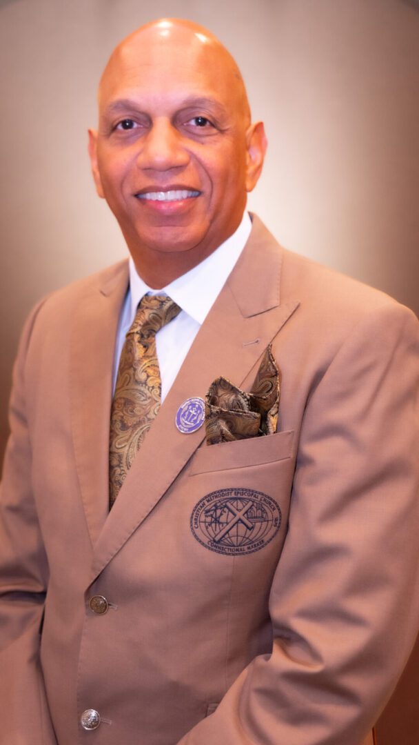 Smiling man in brown suit and patterned tie.